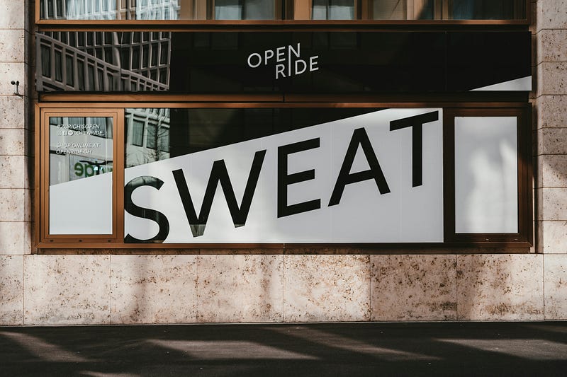 Large storefront window with the word SWEAT in bold black letters across the glass