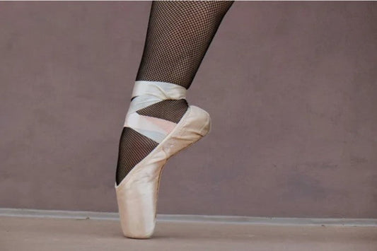 Close up of foot with pink tow ballet shoe on and black fishnet stockings.
