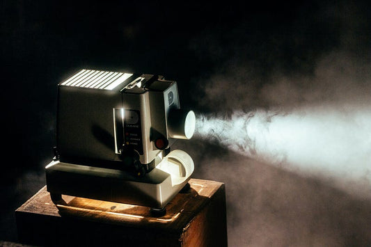 Old movie projector sitting on small table with light shining.